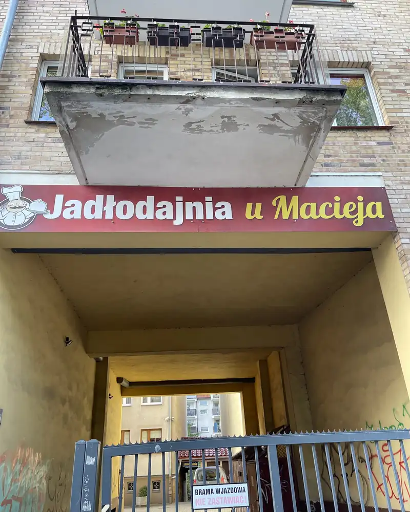Brama z czerwonym szyldem Jadłodajnia u Macieja i balkonem nad wejściem