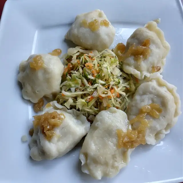 Pierogi z cebulką i surówką z kapusty na białym talerzu